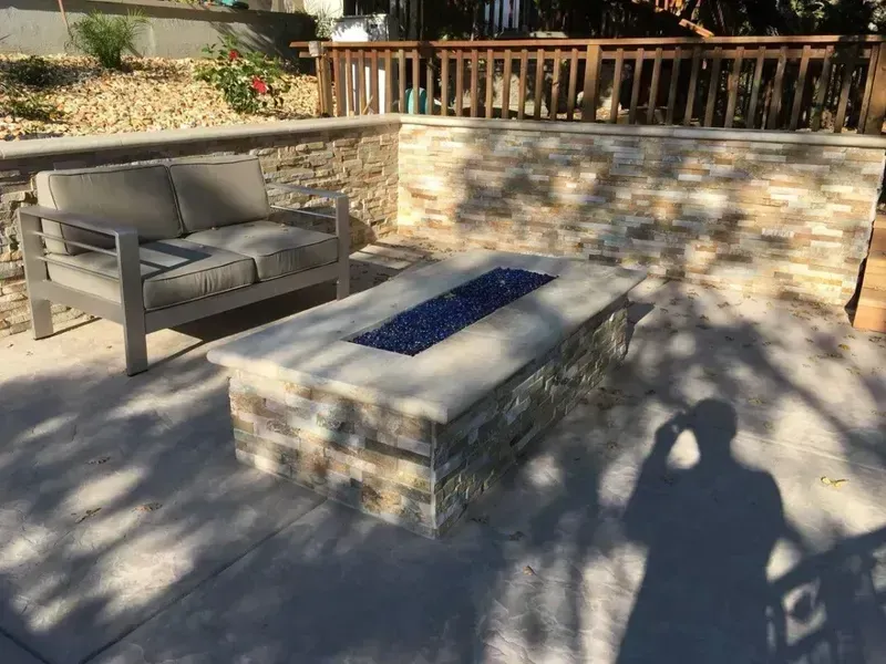 Stone patio with gray bench, concrete fire pit, and wooden railing in sunlight