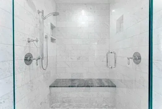 Modern white tiled shower with glass doors, chrome fixtures, and a built-in bench.