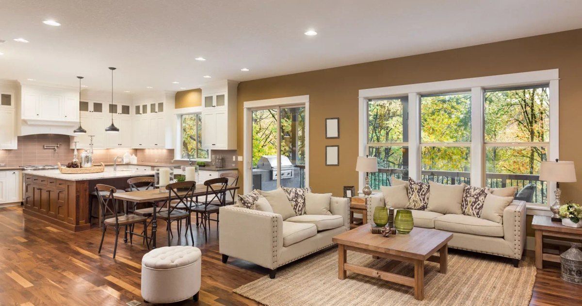 Bright open-plan living room with cream sofas, wooden coffee table, kitchen island, and large windows