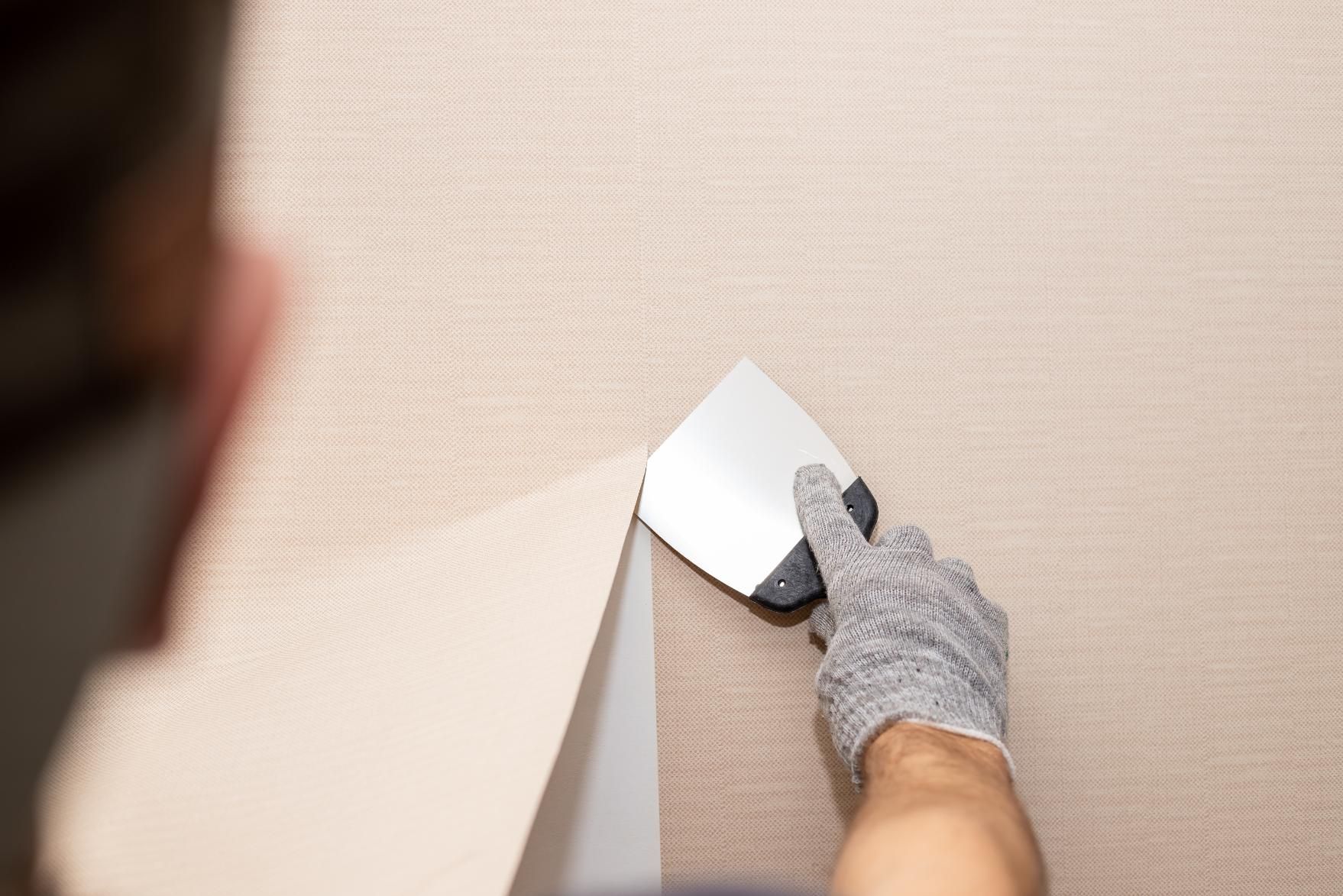 A person is using a spatula to remove wallpaper from a wall.