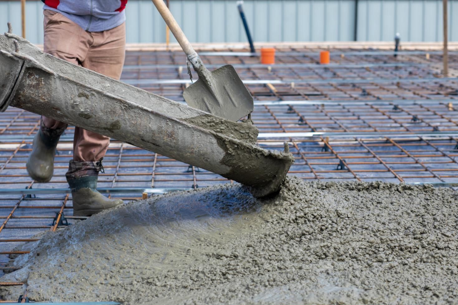A man is pouring concrete into a foundation with a shovel.