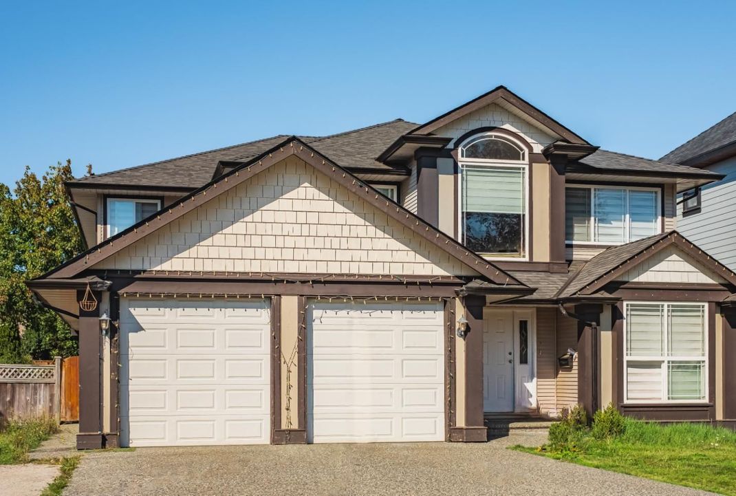 A large house with two garage doors and a blue sky in the background.