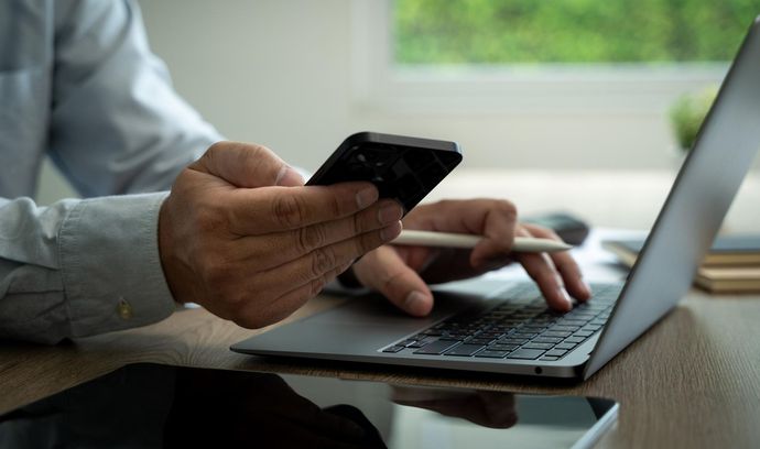A man is using a laptop and a cell phone at the same time.