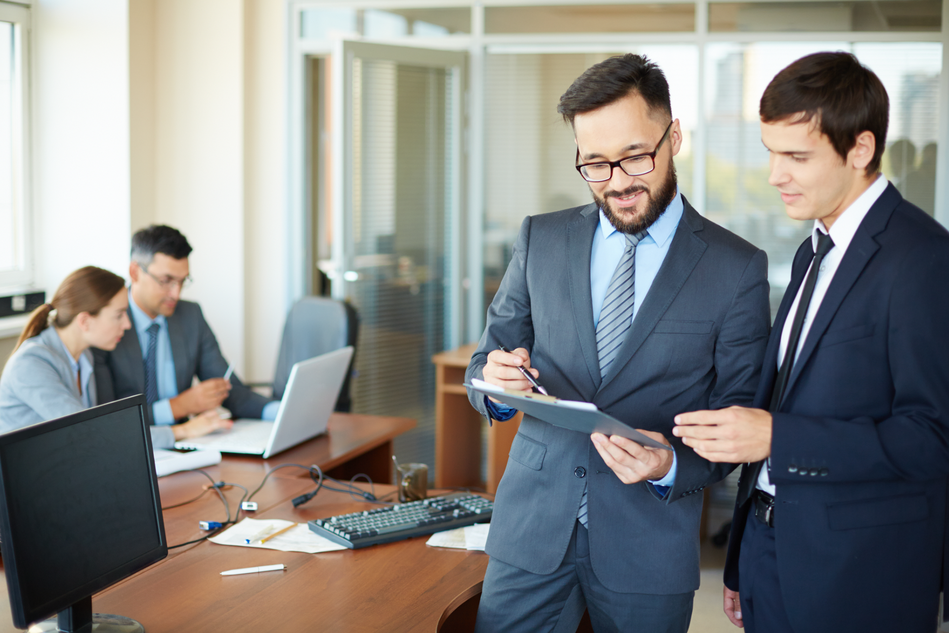 Business professionals collaborate in a modern office, with two people reviewing documents while others work at computers.