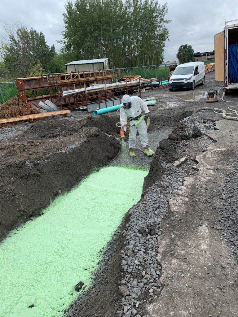 Personne en combinaison de protection debout dans une tranchée remplie de mousse verte, chantier de construction.