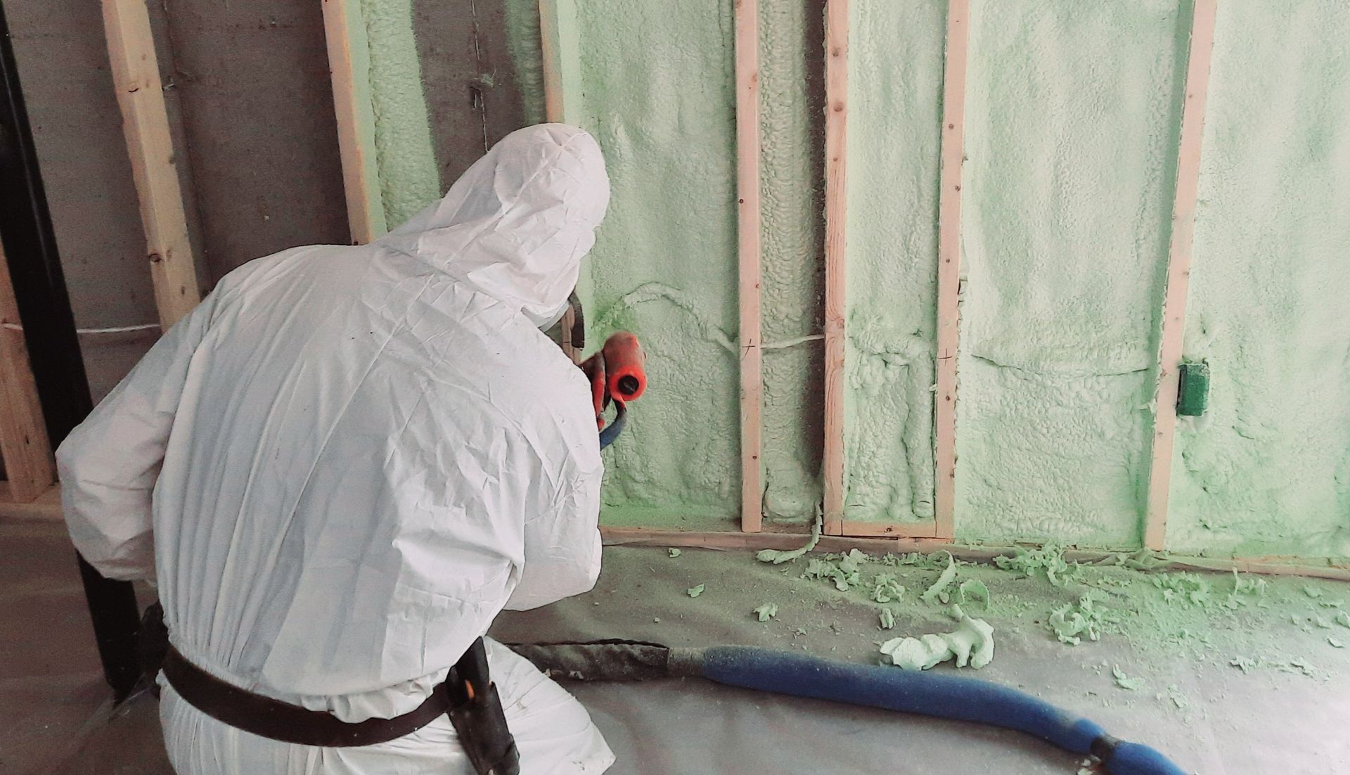 Une personne portant un équipement de protection pulvérise de la mousse isolante verte sur un mur dans un chantier de construction.