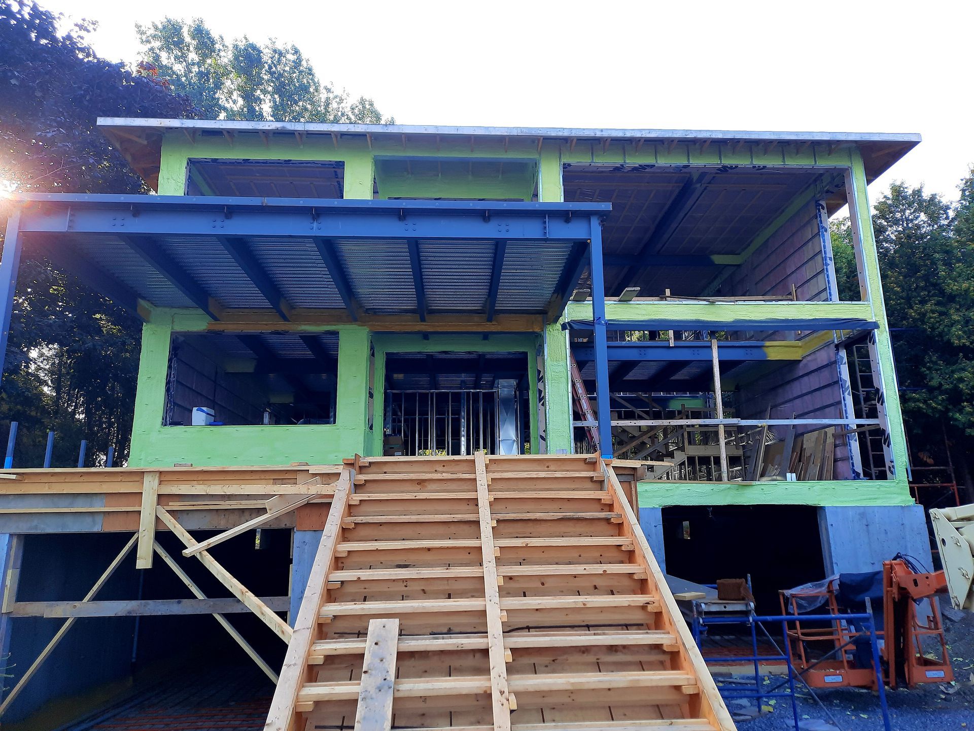 Maison en construction; structure à deux étages avec escalier en bois menant à l'étage, charpente bleue et verte visible.