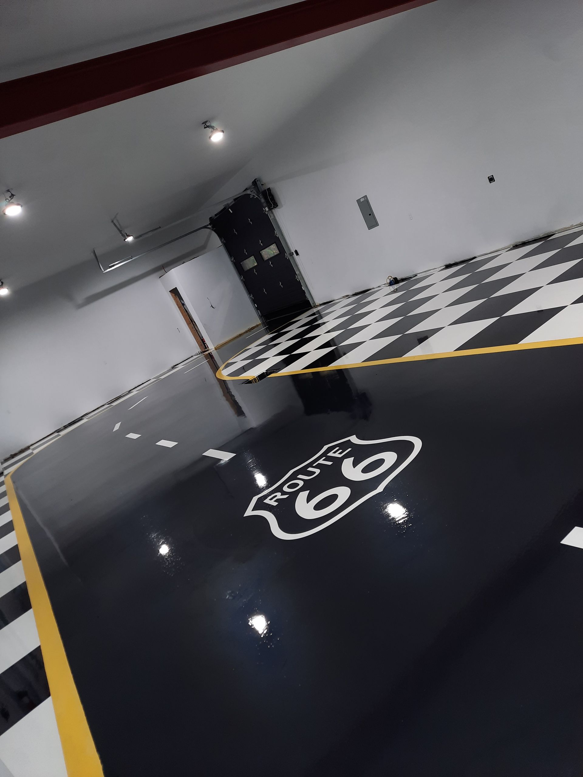 Plancher de garage avec emblème de la Route 66, motif de route et motif à carreaux noir et blanc.