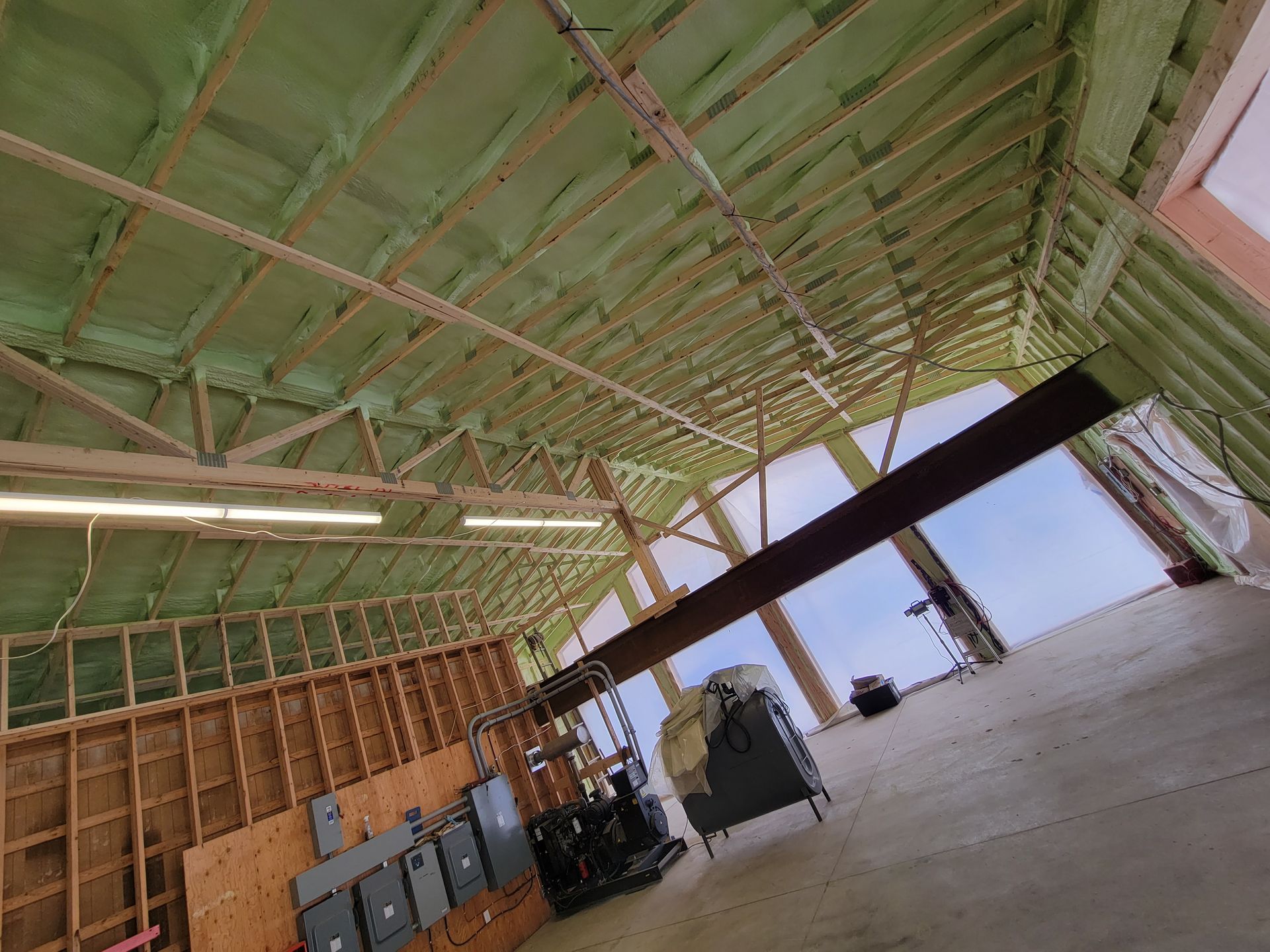 Vue intérieure d'un bâtiment en construction, avec isolation verte, ossature bois et poutre métallique.