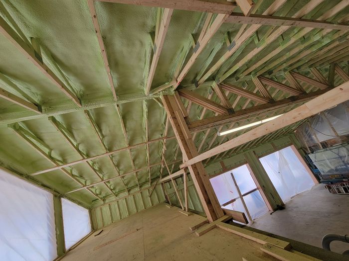 Vue intérieure d'un bâtiment en construction, avec une isolation verte projetée entre les poutres en bois.
