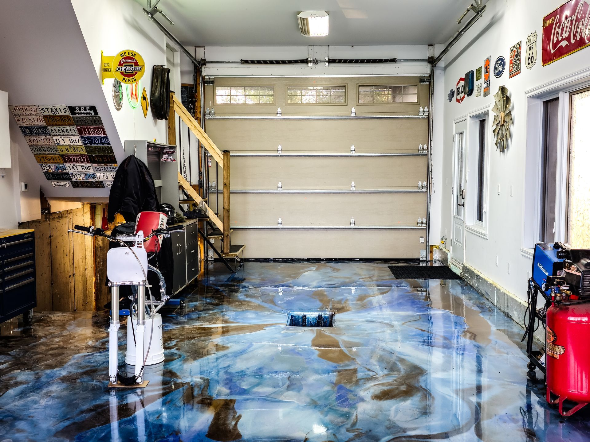 Garage avec plancher en époxy, moto, porte de garage fermée et divers objets sur les murs.