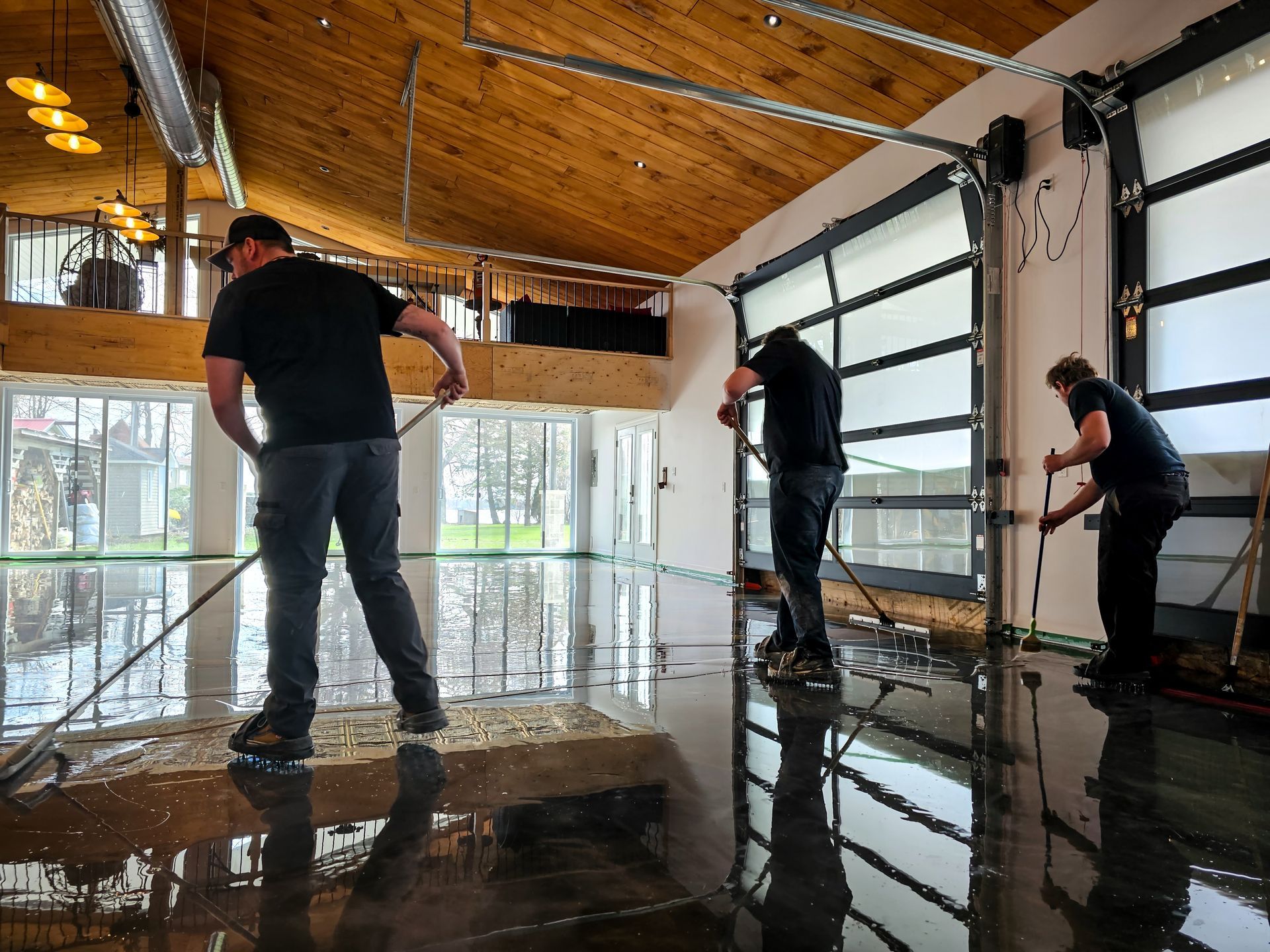 Trois personnes appliquent un revêtement de sol époxy dans un bâtiment moderne avec une porte de garage en verre.