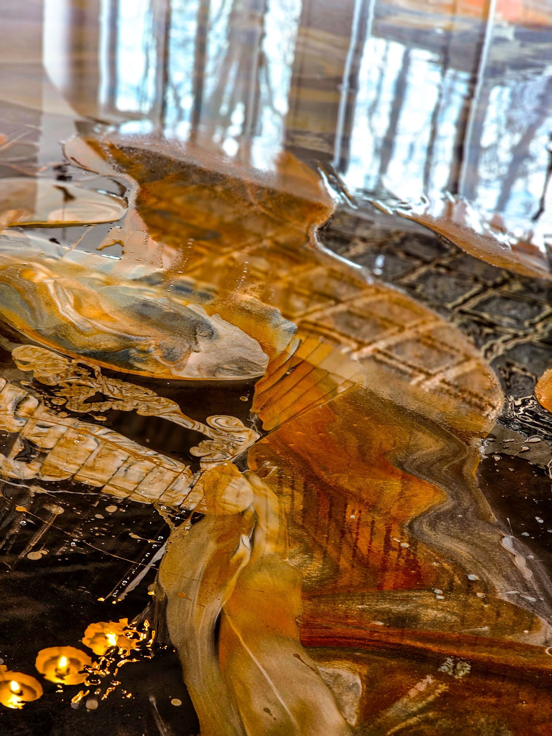 Gros plan d'une œuvre d'art en résine aux couleurs superposées, notamment or, marron et noir, reflétant les arbres.