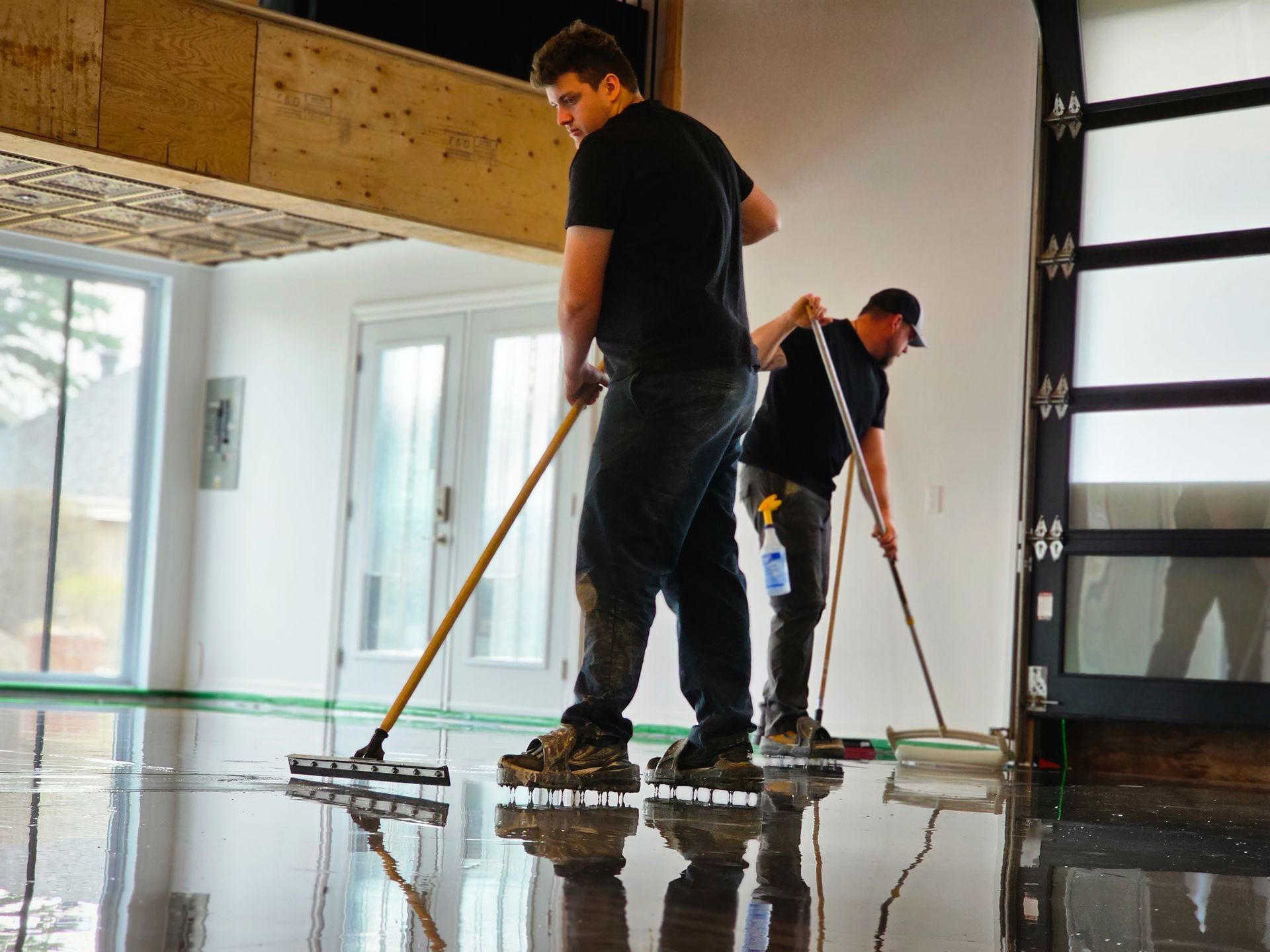 Deux ouvriers appliquent un revêtement de sol époxy; espace intérieur avec fenêtres et porte de garage.