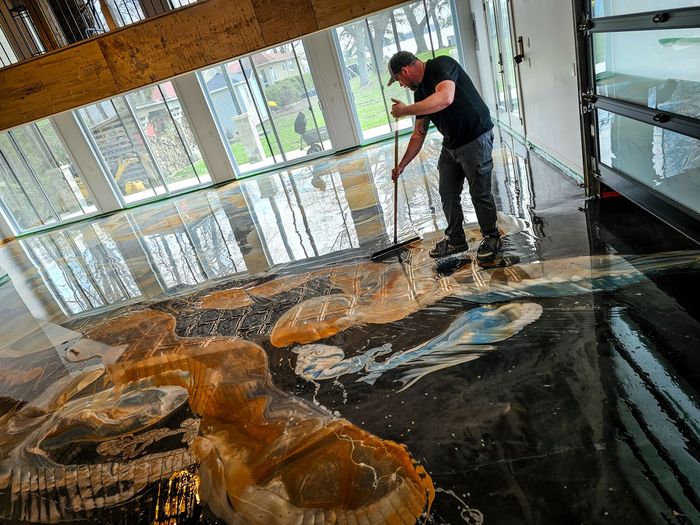 Un homme balayant un sol mouillé avec un design artistique et coloré dans un bâtiment moderne avec de grandes fenêtres.