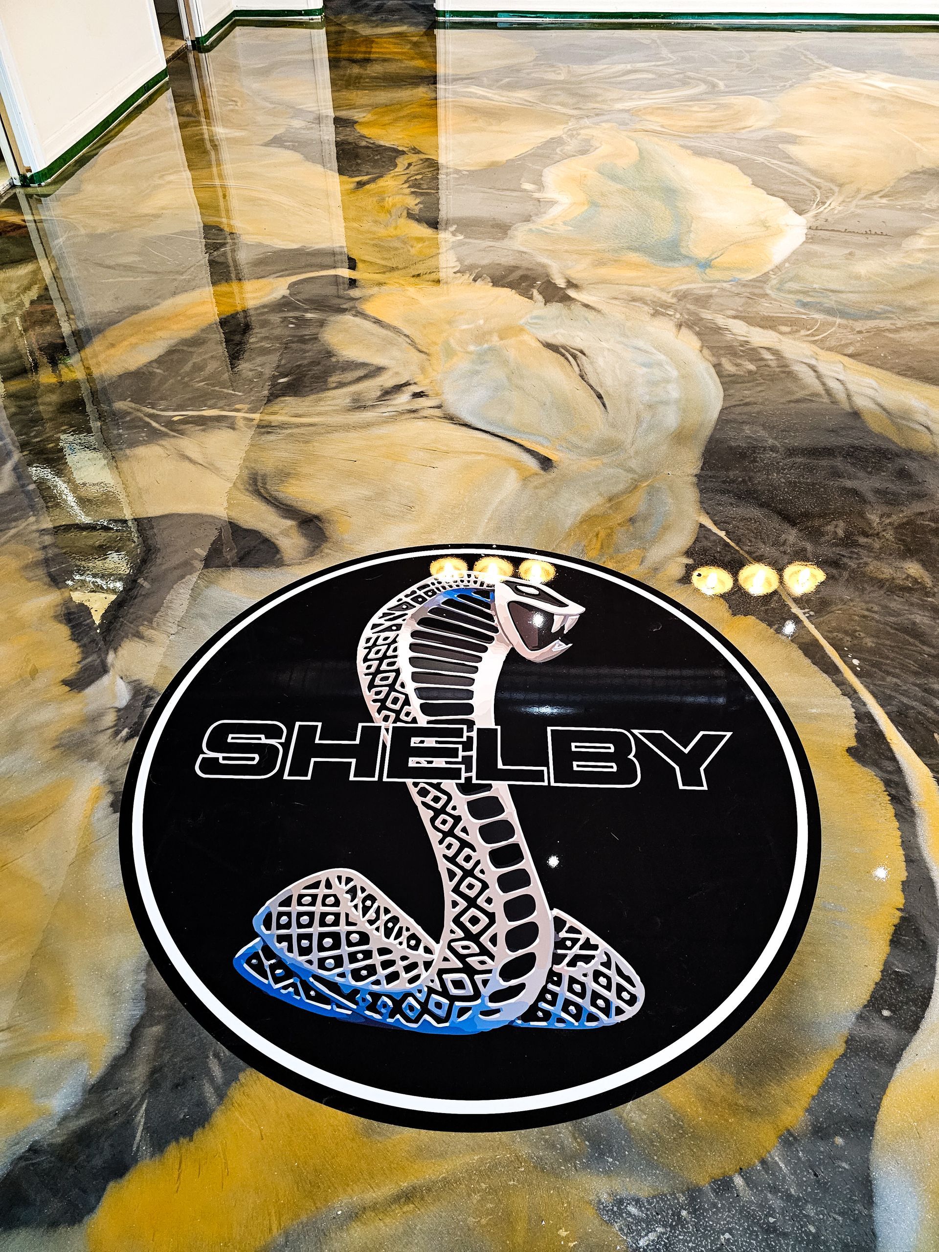 Logo Shelby Cobra sur un sol de garage avec un effet de peinture marbrée.