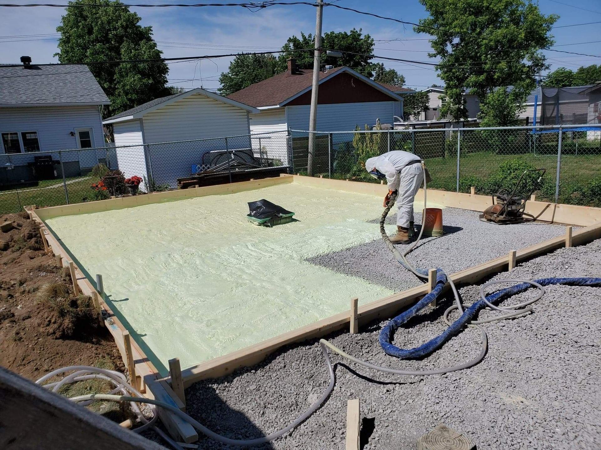 Un homme pulvérise de la mousse isolante dans une fondation en dalle de béton dans une cour arrière résidentielle.