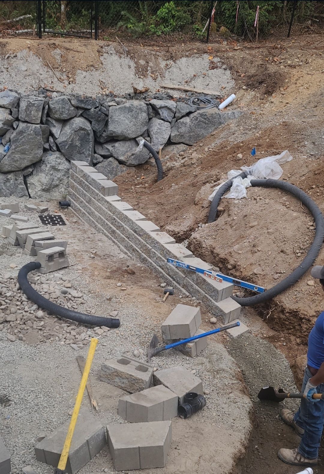 Construction site with retaining wall being built. Blocks and rocks. Person working.