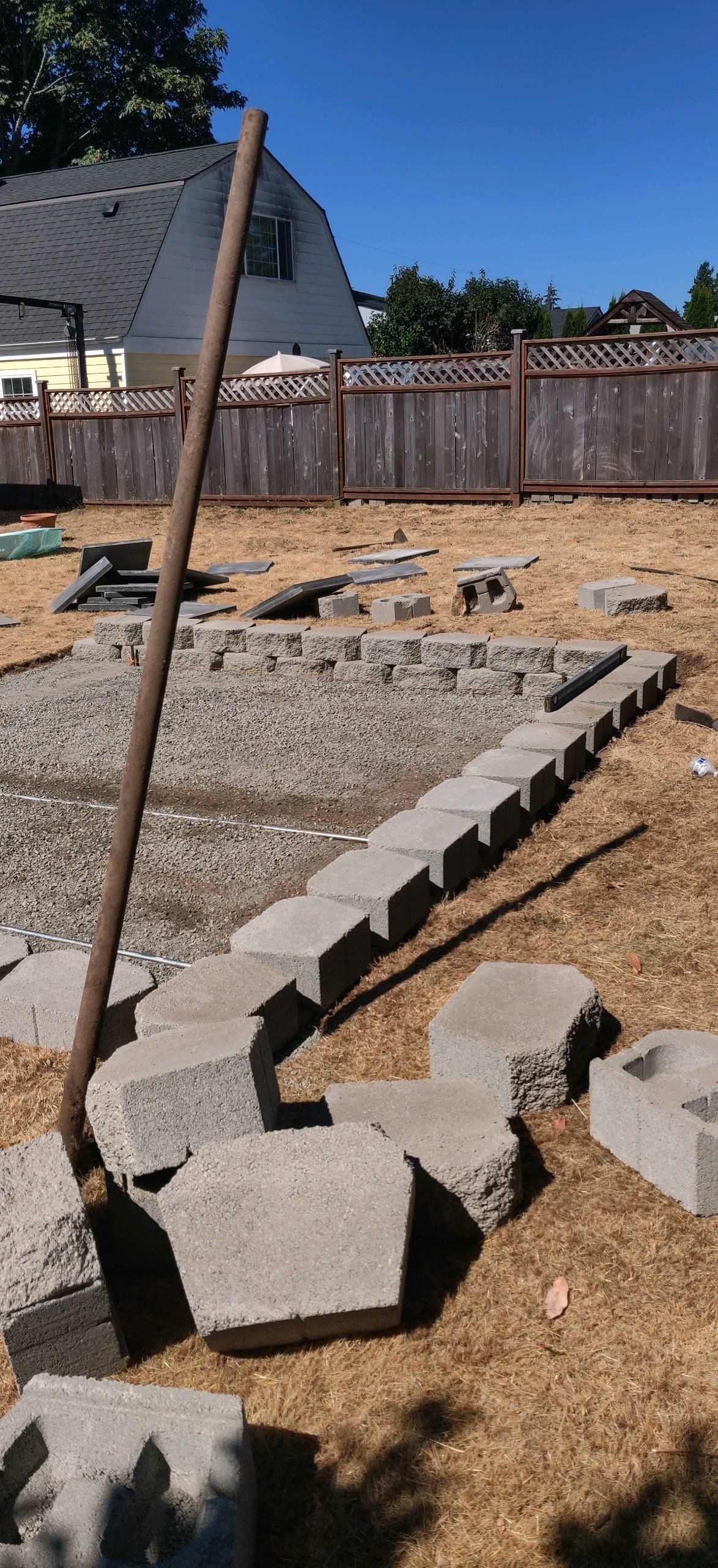 A backyard with gray blocks, a metal pole, and a fence under a clear blue sky.