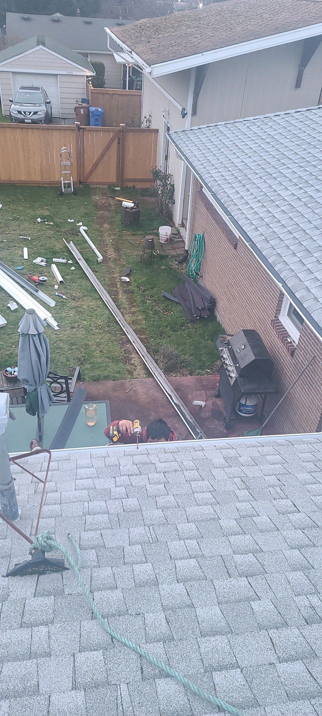 Overhead view of a suburban backyard with a wooden fence, lawn, and a ladder leading toward a brick house.