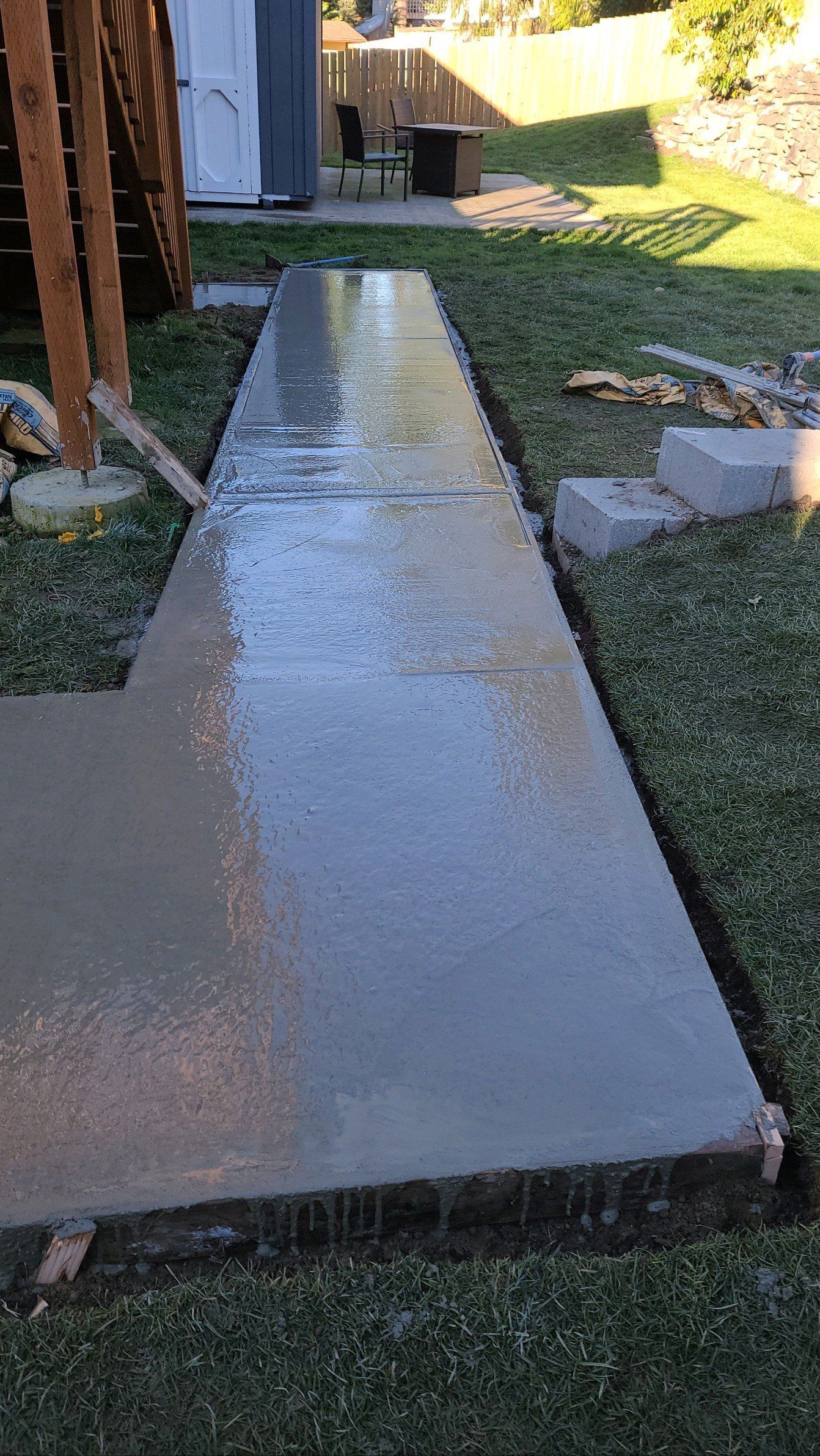 Freshly poured concrete walkway in a backyard, bordered by grass and wooden forms.