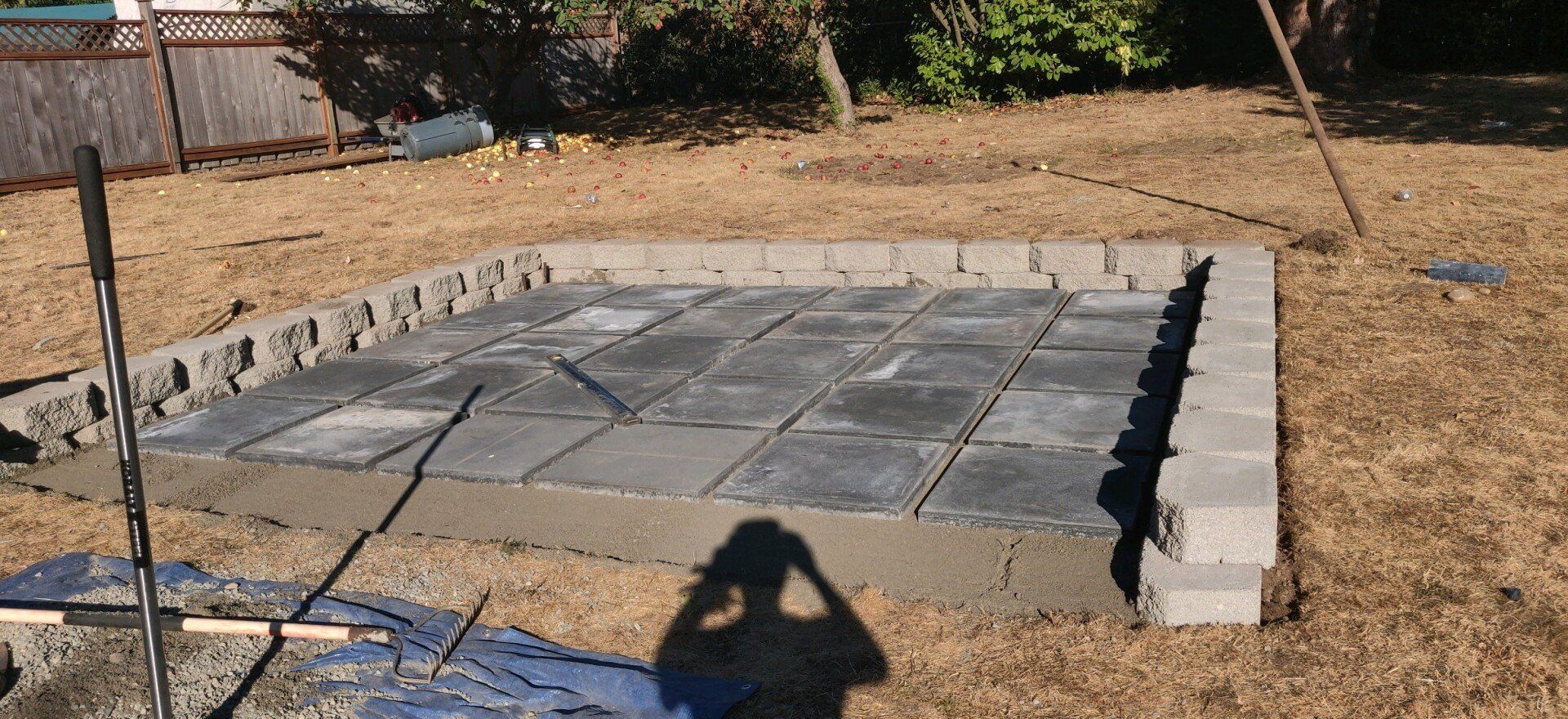Construction of a rectangular patio base in a backyard; gray blocks form the border, concrete paving stones within.