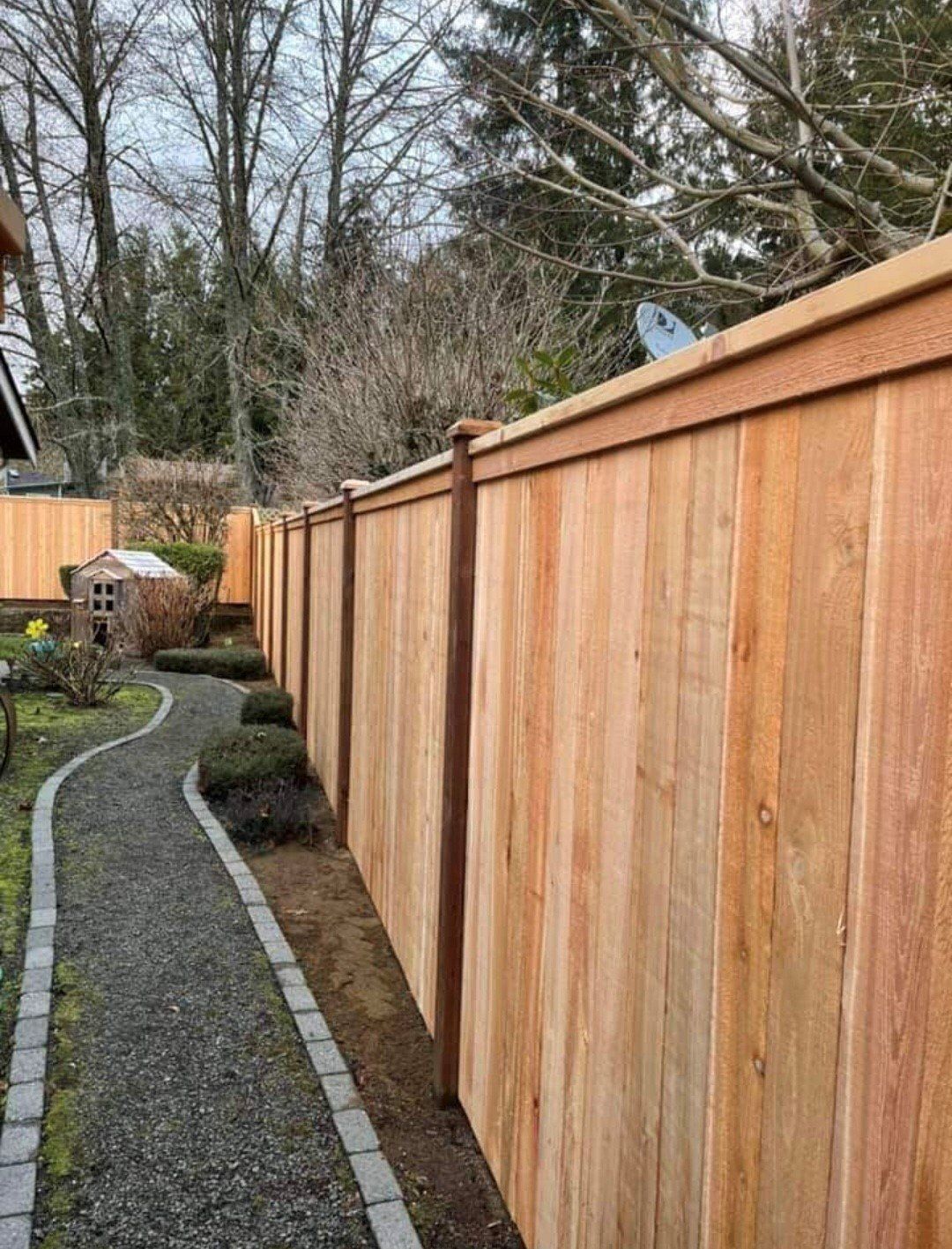 Wooden fence in a yard with a gravel path leading to a small shed.