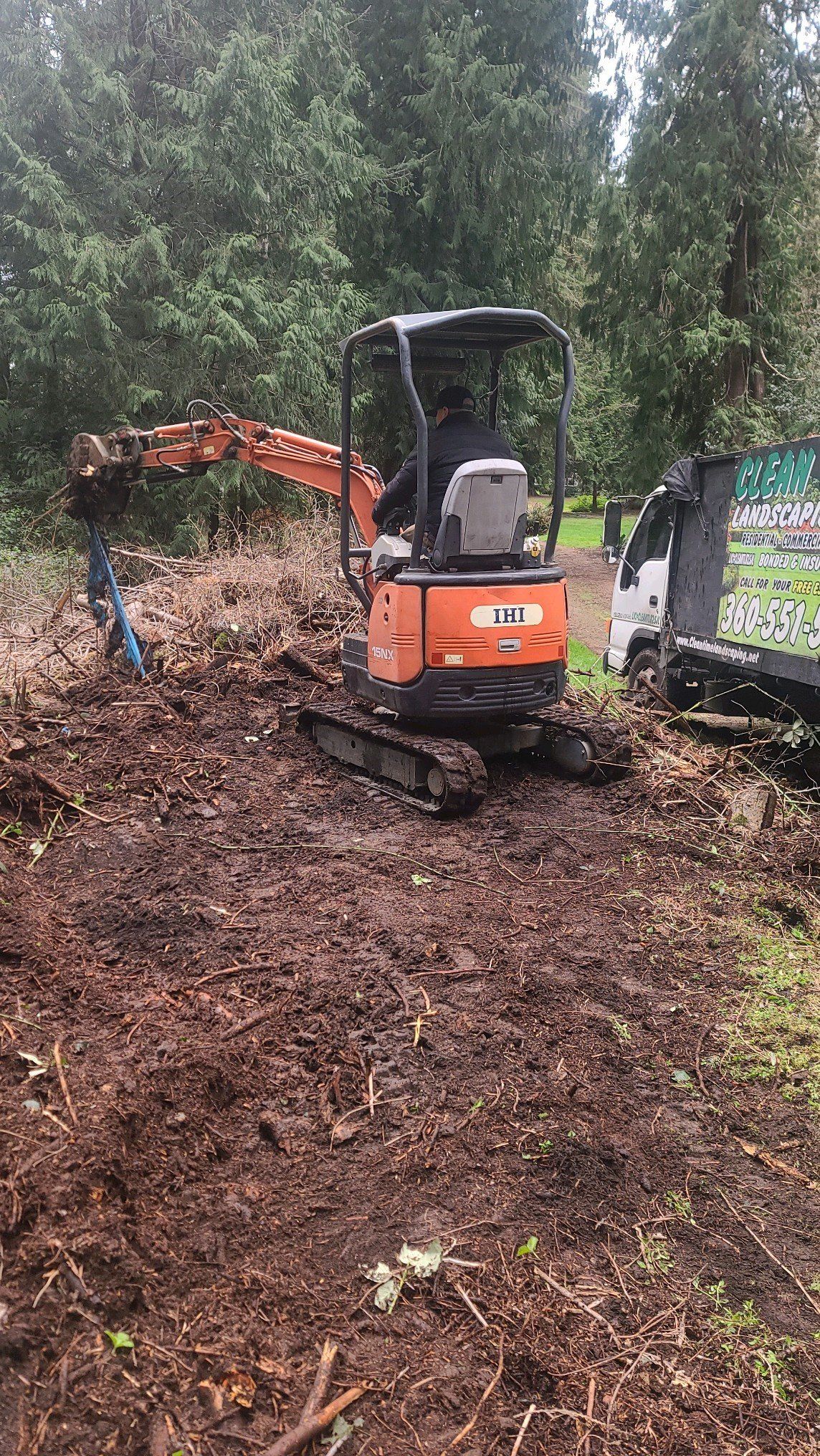 Orange mini excavator digging in dirt with a person operating it. Trees are in the background.