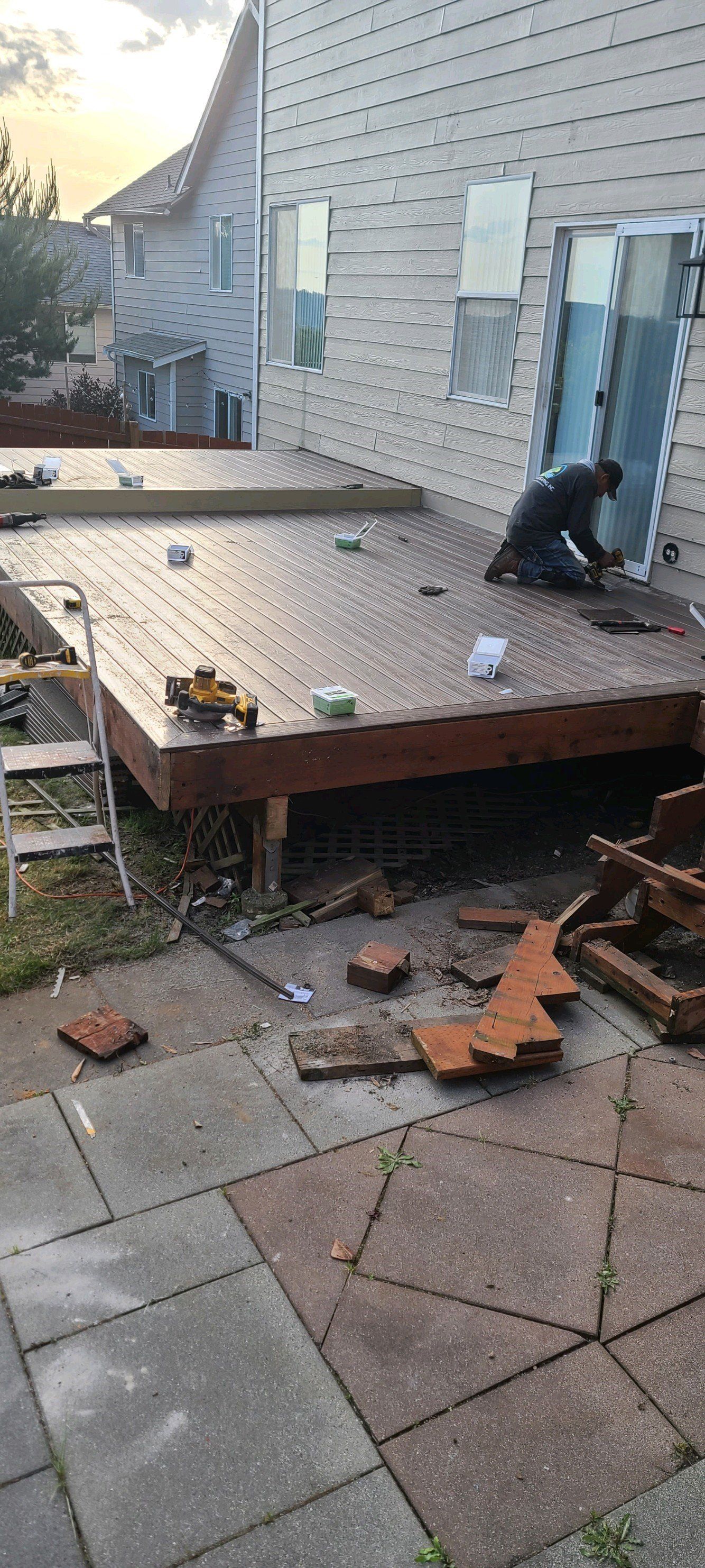 Person working on a deck attached to a house. Bricks scattered on the patio below.