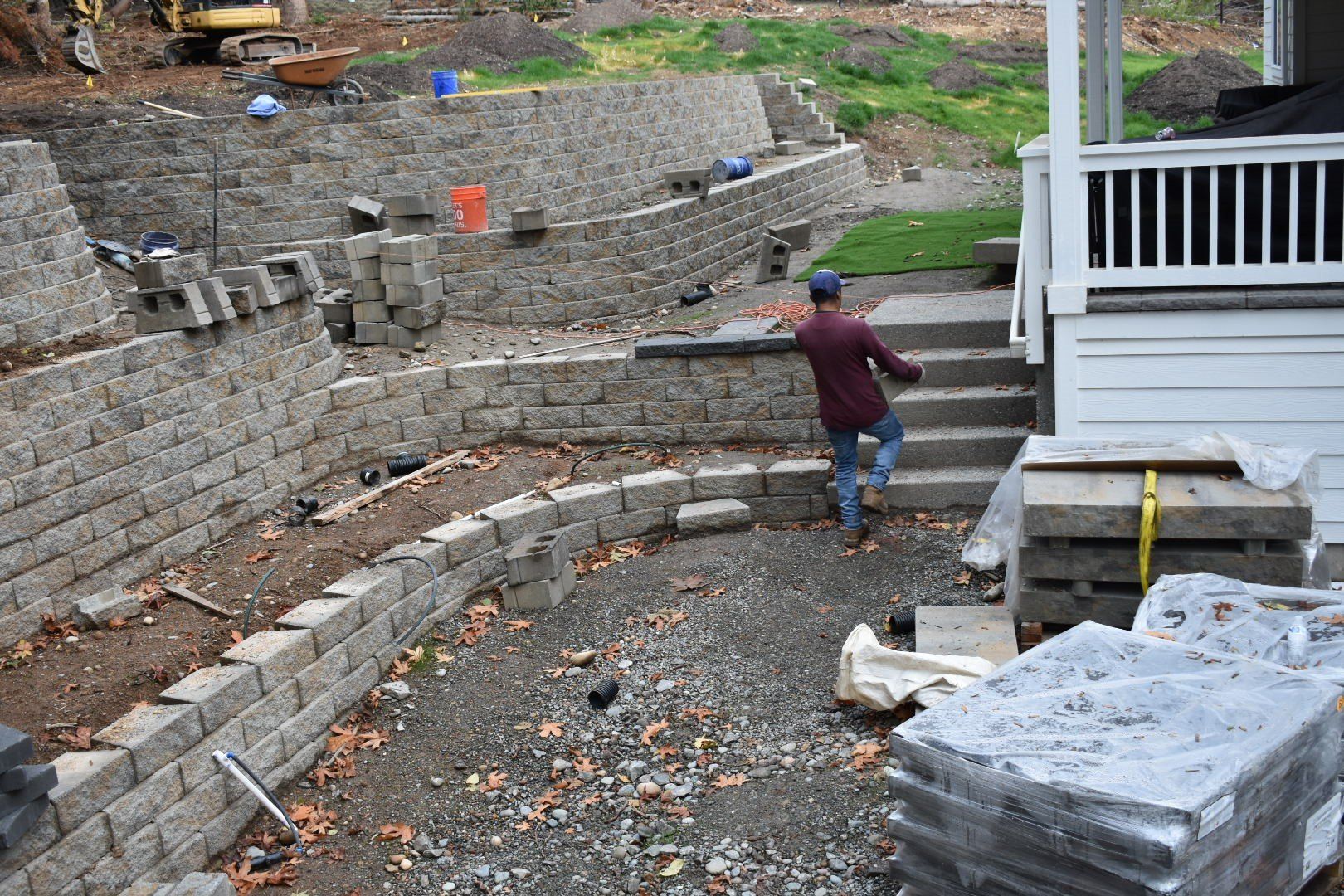 Construction site with retaining walls, steps, and a person walking towards a house.