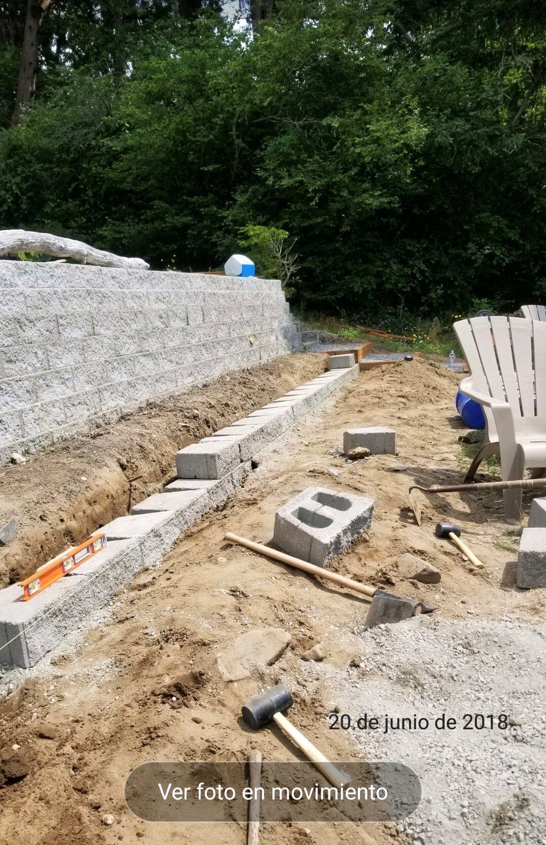 Construction site: laying cinder blocks for a wall, with a gravel backdrop and trees.