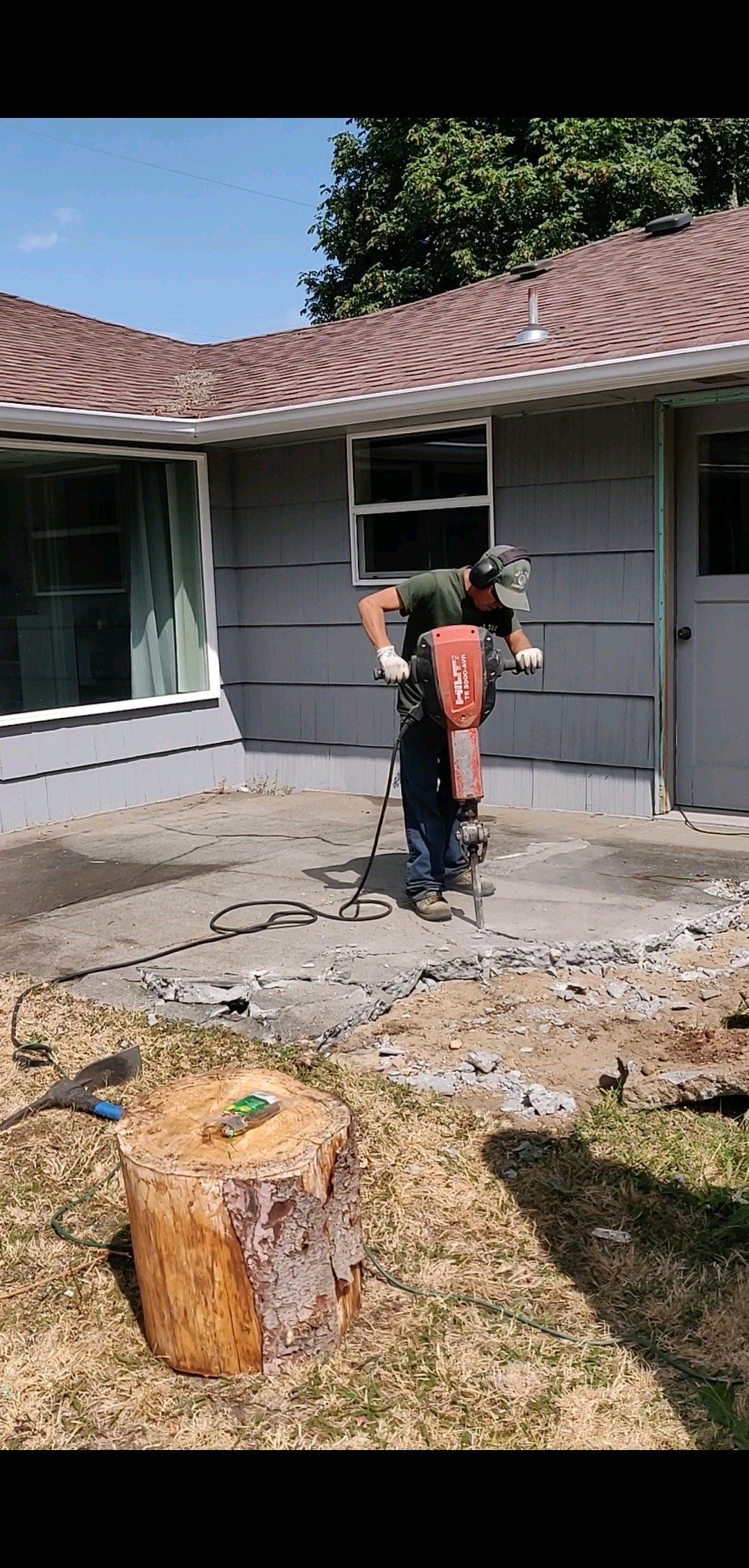 Person using a jackhammer on a concrete surface outside a house.
