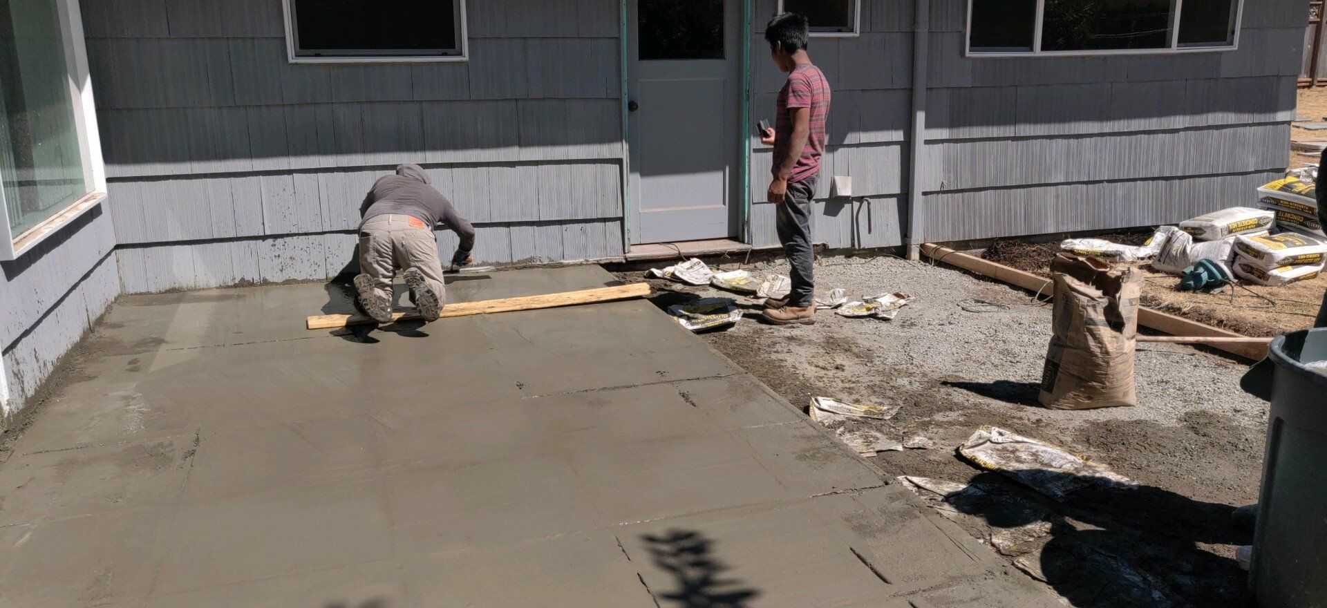 Two workers pouring concrete outside a building. One levels the wet concrete. The other watches.