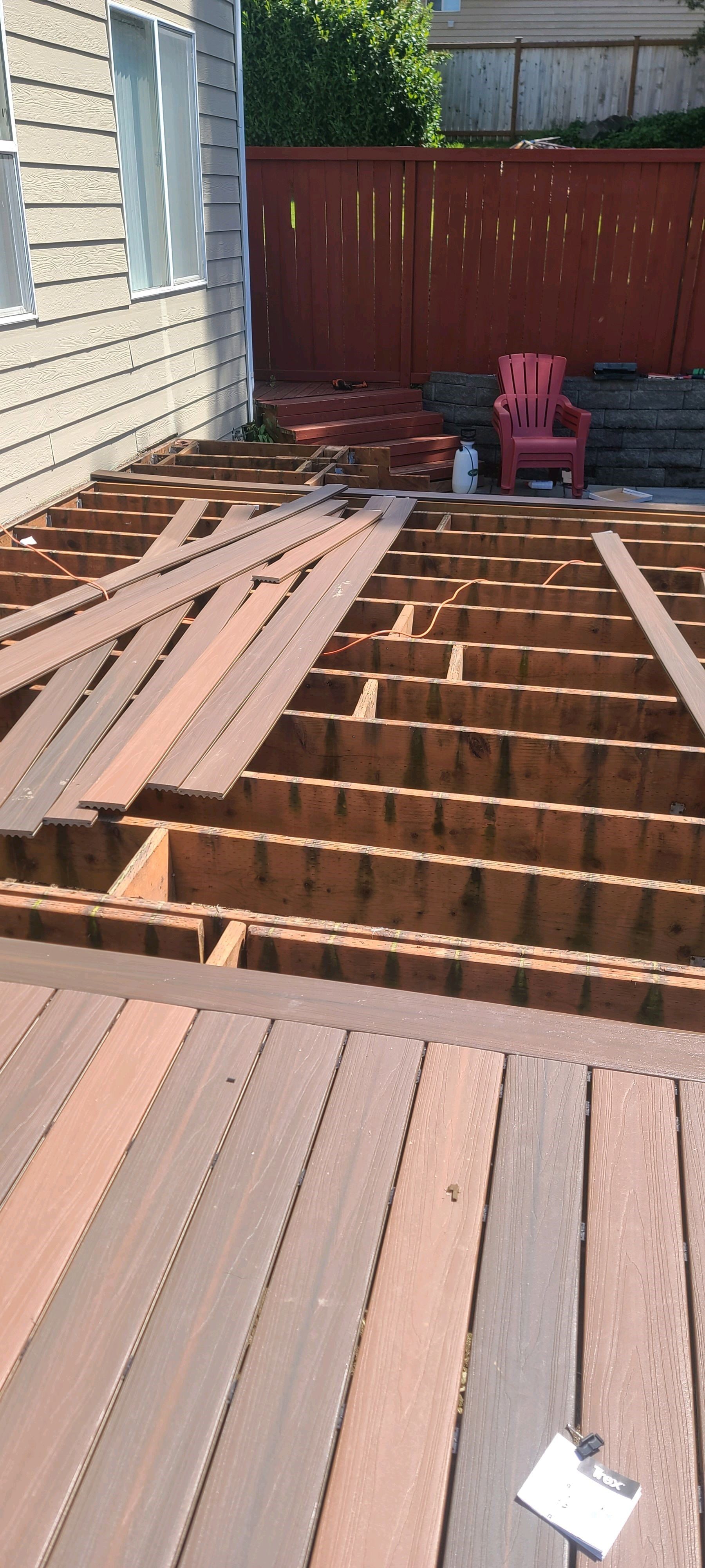 Deck under construction; wooden planks removed exposing the frame. Red chair and fence in the background.