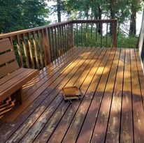 Wooden deck with bench, railing, and a small, square object. Sunlight hits the boards.