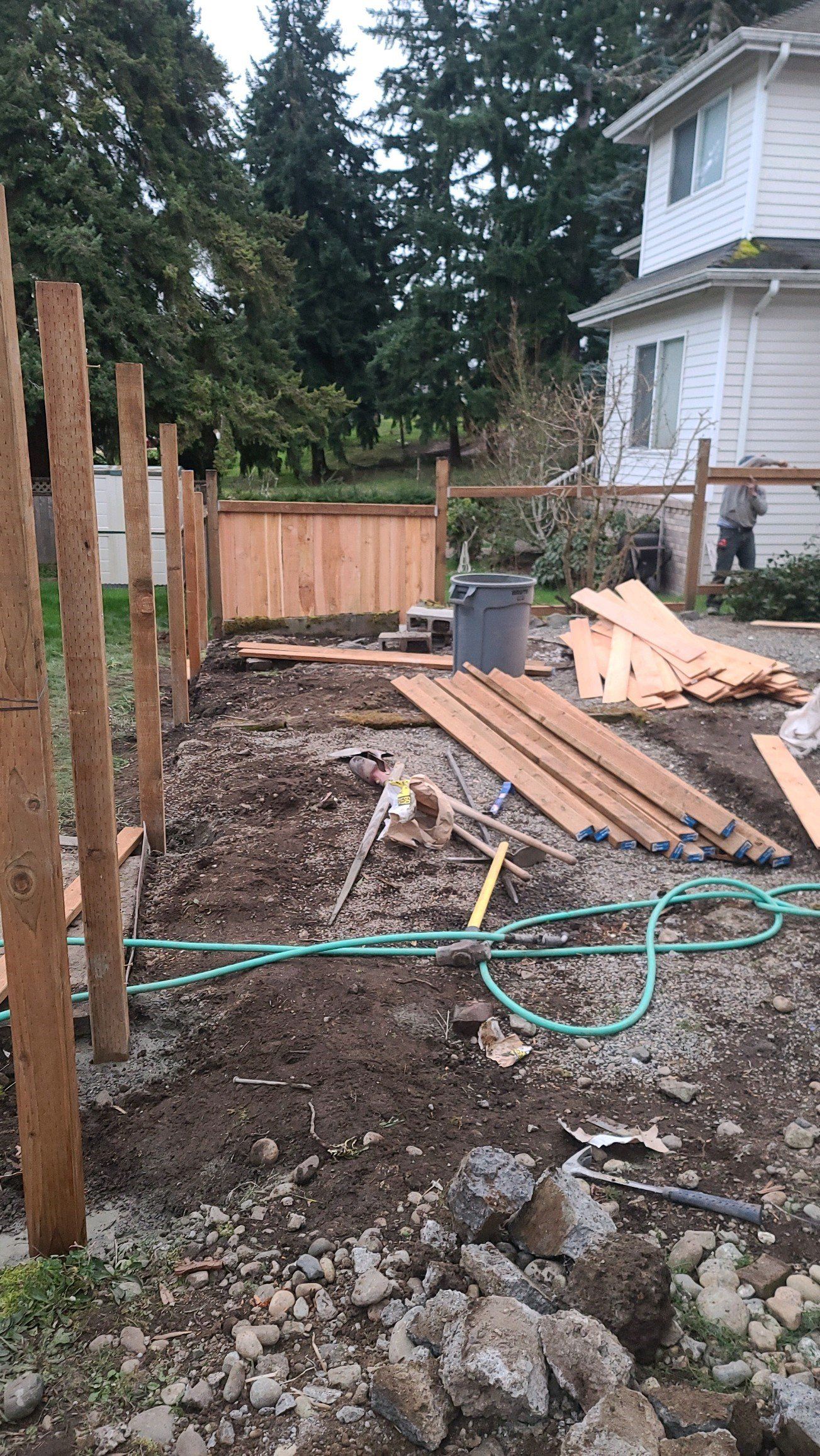 Fence construction in progress: wooden posts, planks, tools, and dirt.
