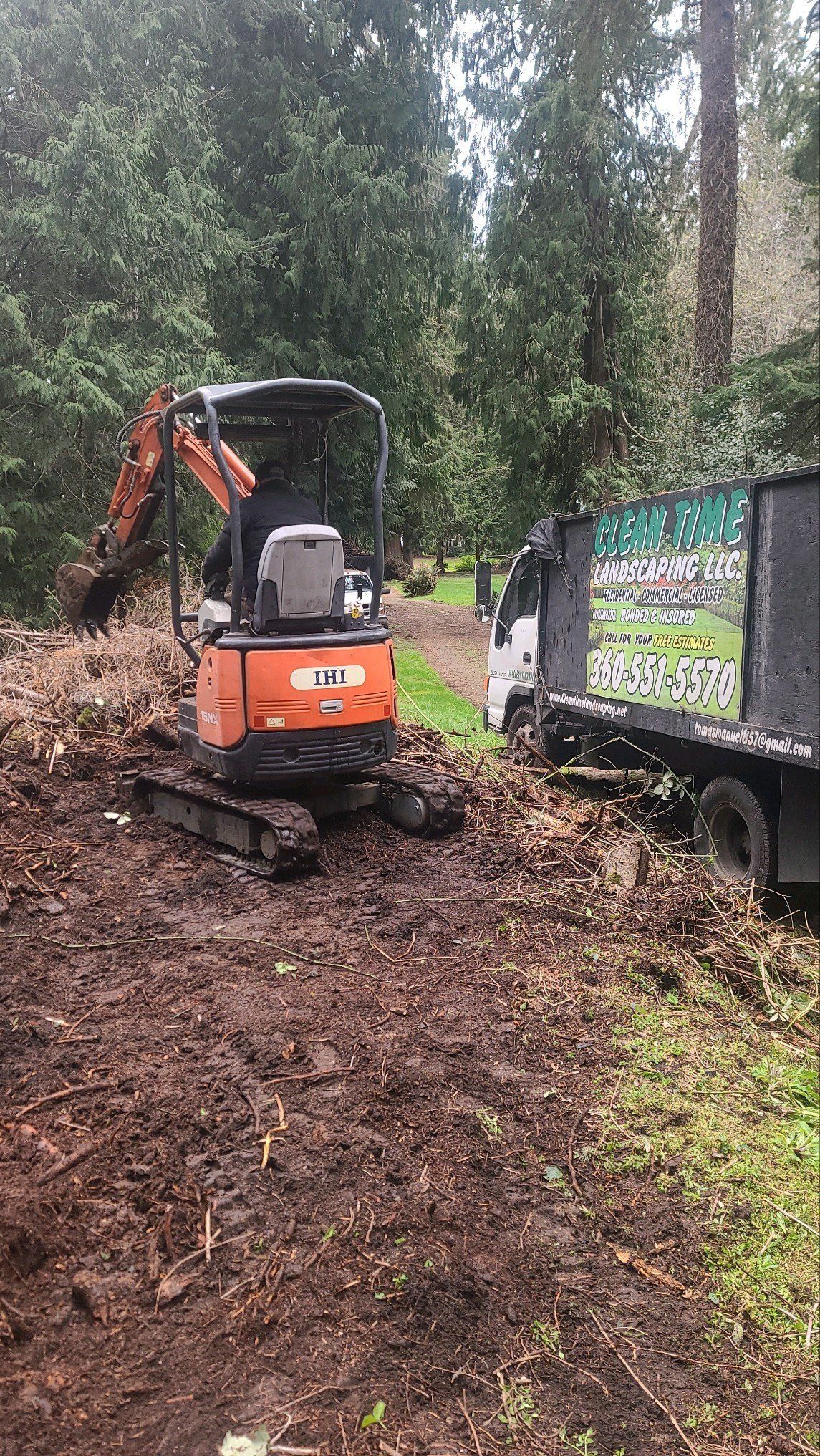 Mini excavator loading debris into a dump truck in a wooded area.