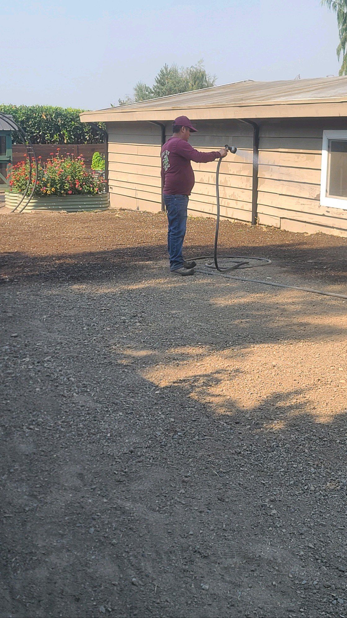 Person spraying a gravel driveway next to a building on a sunny day.