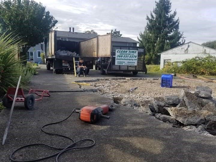 A demolition site. Workers and a truck removing debris from broken pavement. Power tools sit nearby.