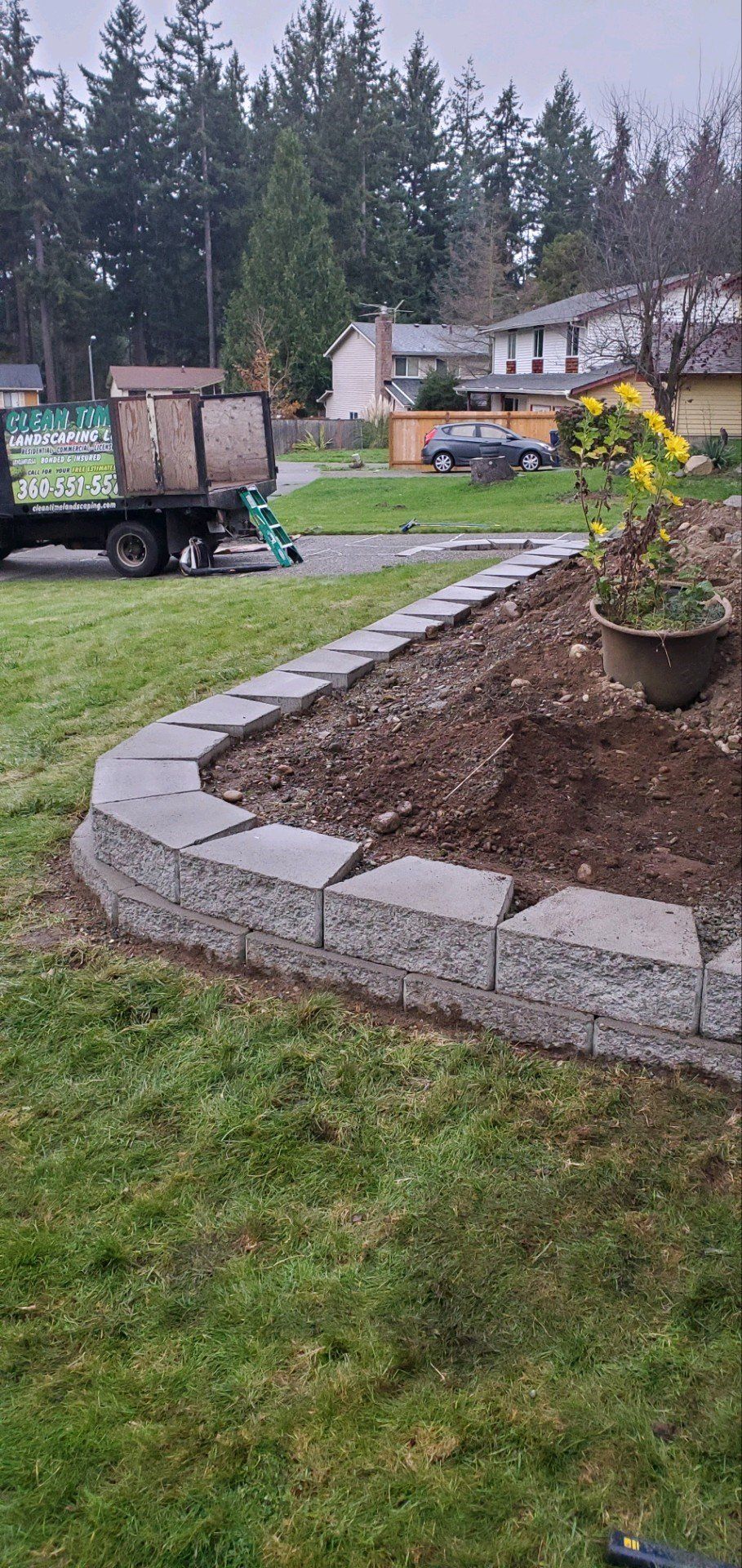 Landscaped yard with retaining wall, dirt and grass. A truck is parked in the background.
