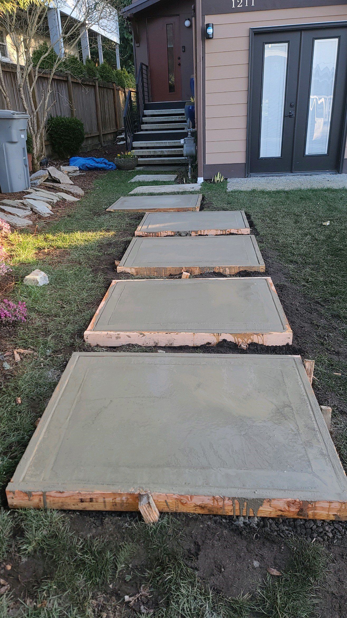 Concrete stepping stones in a grassy yard leading to a house with steps. Wooden borders visible.