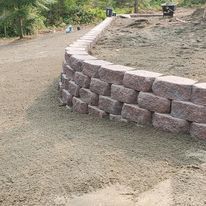 Retaining wall of reddish-brown blocks curves along a gravel path.