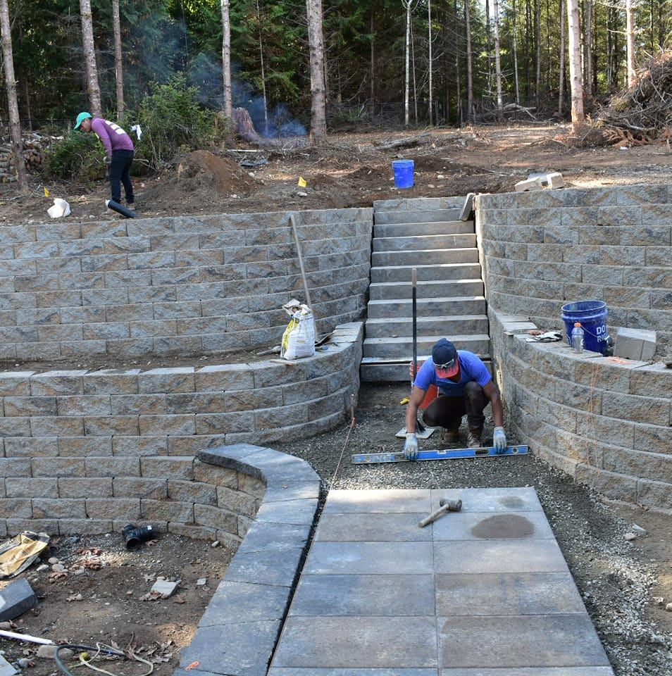 Construction workers building a stone staircase and retaining walls on a hillside.