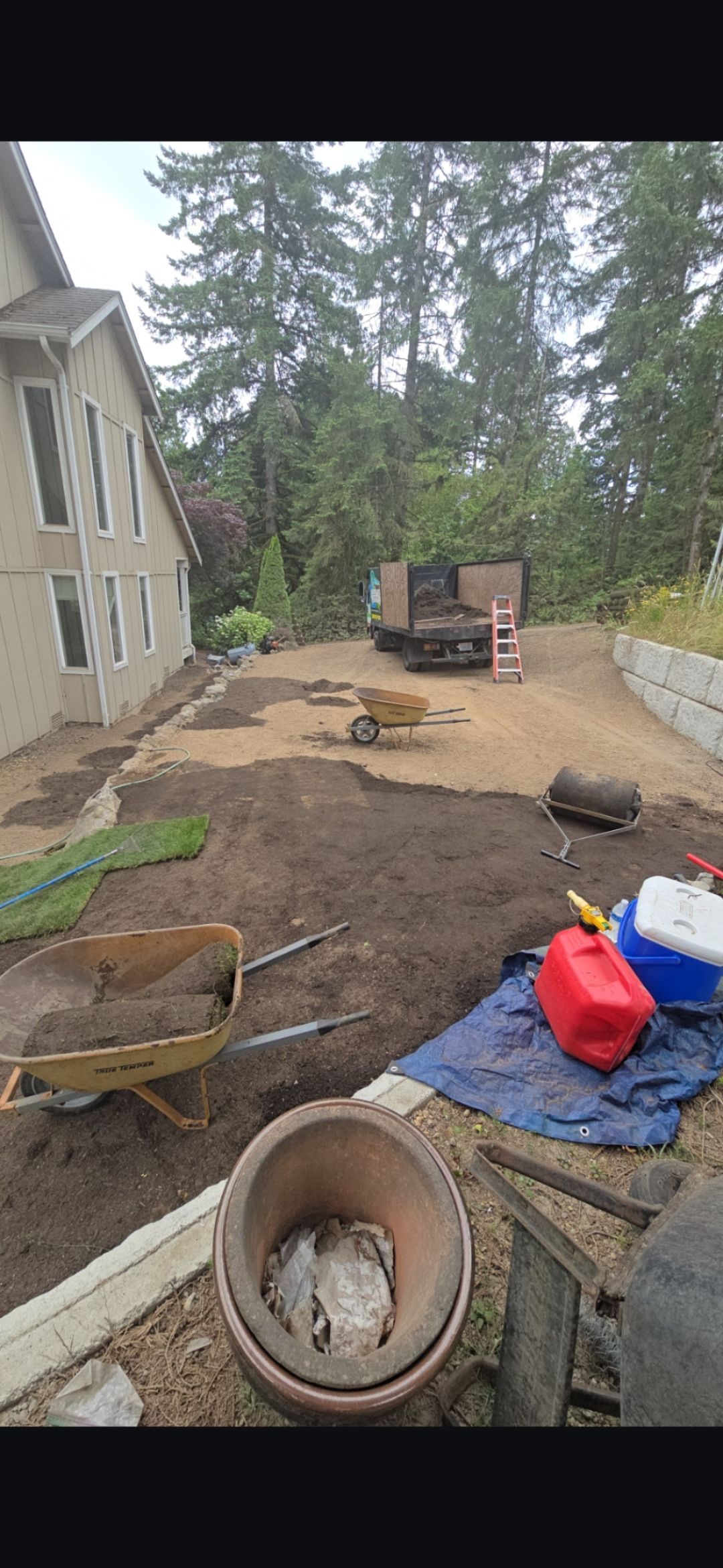 A residential yard under construction, with a house on the left, a truck in the middle, and tools scattered.