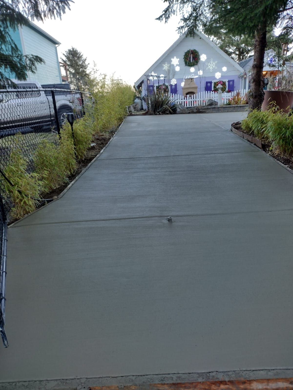 Concrete driveway leading to a white building decorated for an event, lined with green bushes.