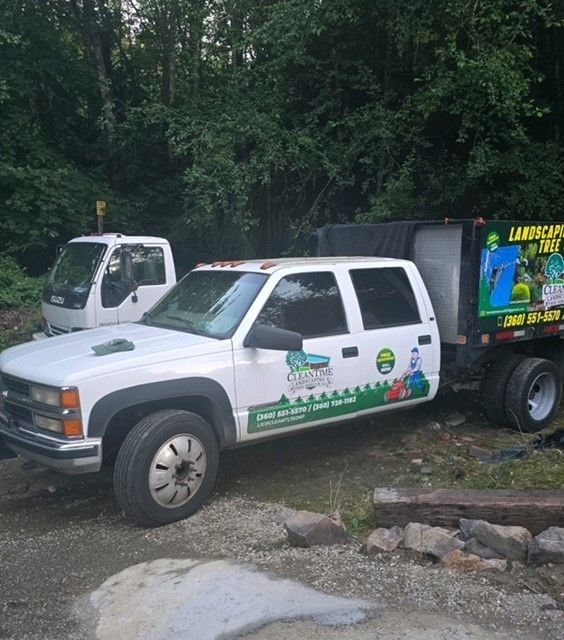 White landscaping trucks parked near trees. One truck has a trailer with landscaping logo.
