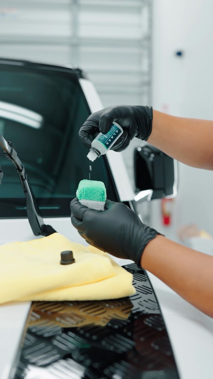 Gloved hands applying polish to a car hood in an auto detailing shop