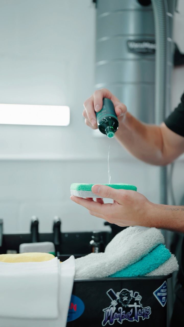 Person squeezes green liquid onto a sponge near a bathroom sink.