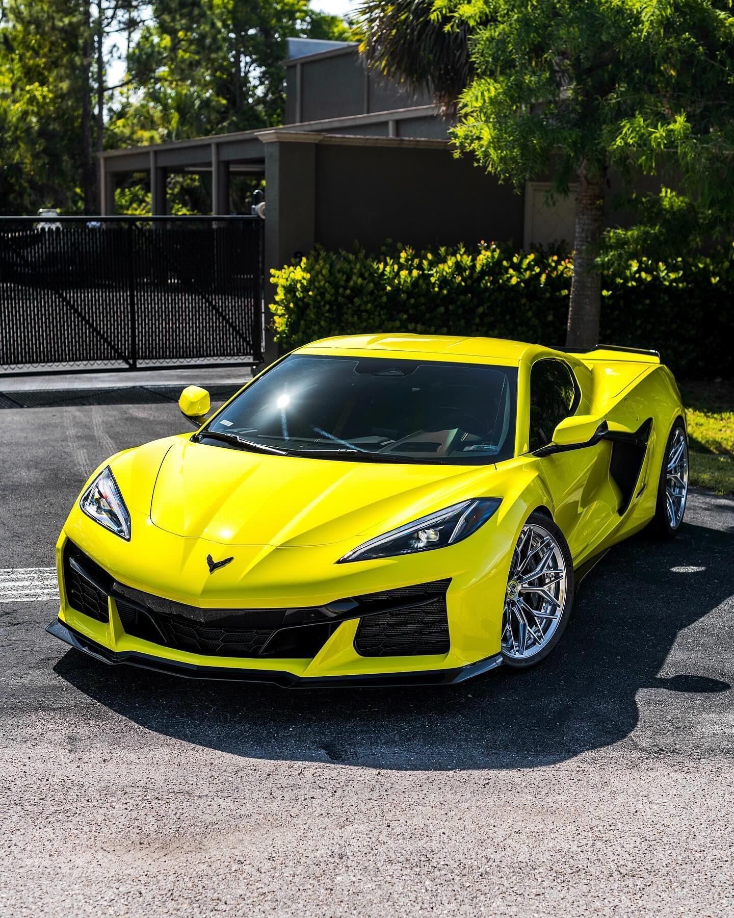 Bright yellow sports car parked on a driveway in front of a house and trees