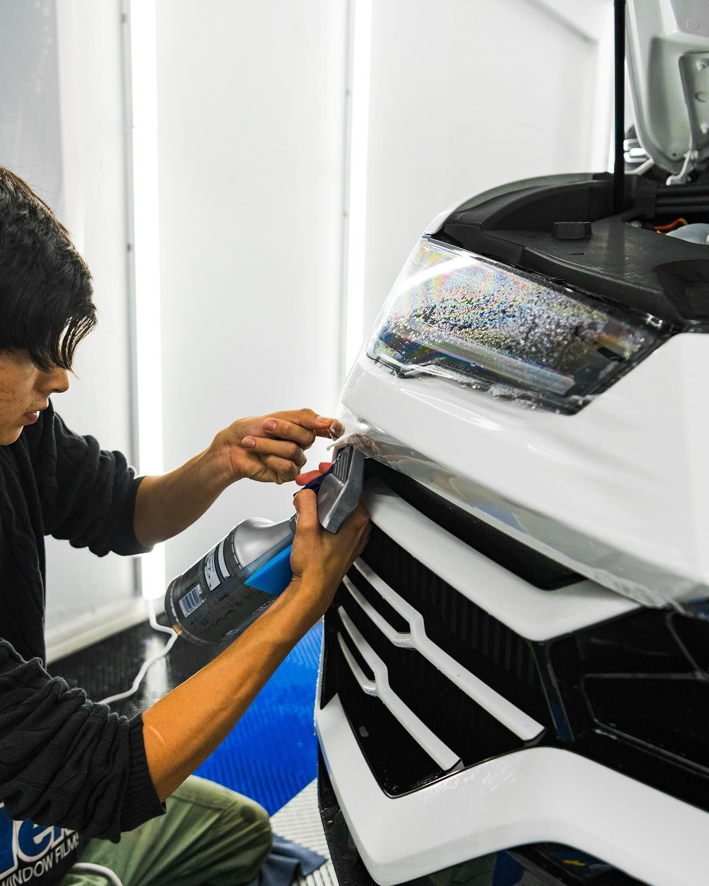 Person applying film to the headlight of a white car in a workshop
